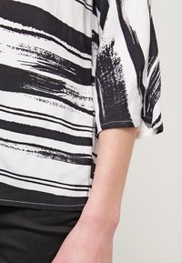 Blouse rayée noir et blanc à coupe fluide et manches trois-quarts, fabriquée dans un tissu lisse au toucher doux.