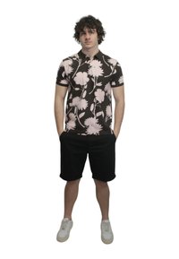 Polo a maniche corte con una base marrone scuro decorata con grandi motivi floreali rosa, abbinato a pantaloni corti neri e sneakers bianche.