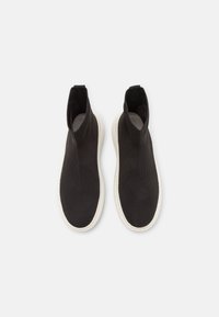 Paire de baskets noires en maille sans lacets avec col haut autour de la cheville et semelles blanches, présentées vues de dessus sur fond blanc.