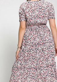 Robe fleurie présentant un design à volants avec un motif de fleurs blanches, rouges et noires sur un fond clair, manches courtes et taille élastique.