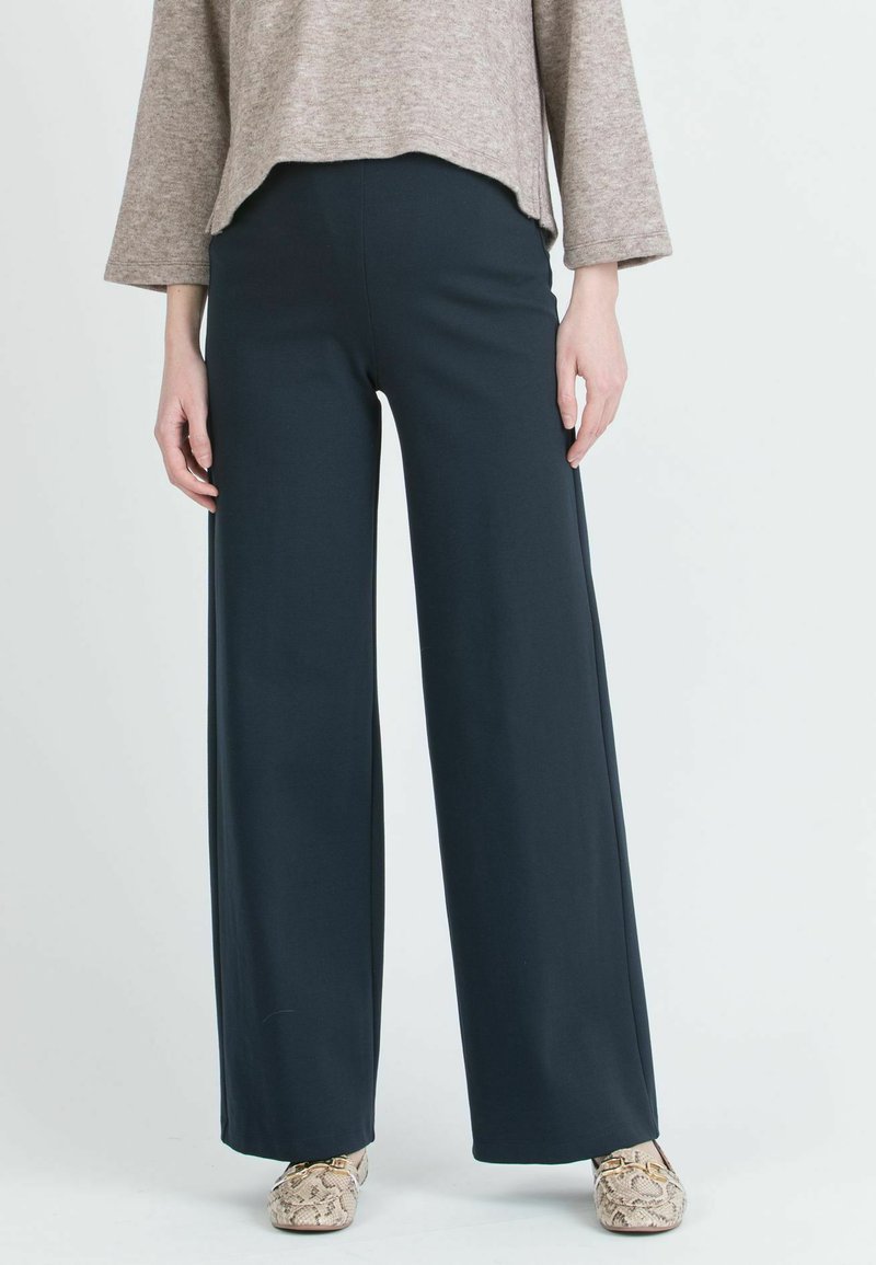 Tumma siniset, leveälahkeiset housut pehmeästä kankaasta, jossa on sileä pinta. Yhdistetty vaaleanruskean yläosan ja kuvioitujen kenkien kanssa.