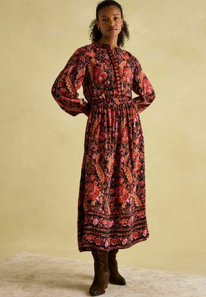 Black floral maxi dress with long sleeves and gathered waist, featuring vibrant pink and orange patterns, and a button-up front. Brown boots.