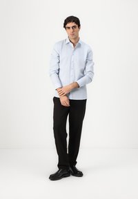 Cămașă albastru deschis, cu textură netedă, mâneci lungi și guler ascuțit, asortată cu pantaloni negri și pantofi negri.