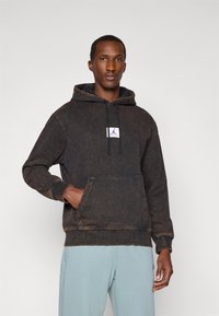 Black and brown tie-dye hoodie with a front pocket, drawstring hood, and a purple logo patch on the chest. Soft fabric with ribbed cuffs.