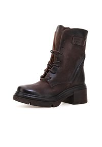 Brune læder ankelstøvle med snørebånd, kraftig sål, blokhæl, sidepanel-accenter og et lille rektangulært mærke på skaftet.