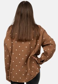 Brown, checked button-up shirt with white heart patterns, long sleeves, relaxed fit, and a textured fabric. Viewed from the back.