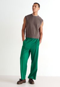 Top sin mangas marrón y pantalones de satén verde de pierna ancha. Calzado marrón con suela gruesa. Diseño simple con un corte relajado.