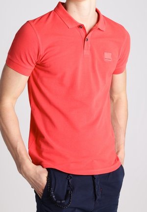 Rotes Poloshirt aus Baumwolle mit Kragen, Zwei-Knopf-Leiste und kleinem Logoaufnäher auf der linken Brust. Kurzärmlig und figurbetont geschnitten.