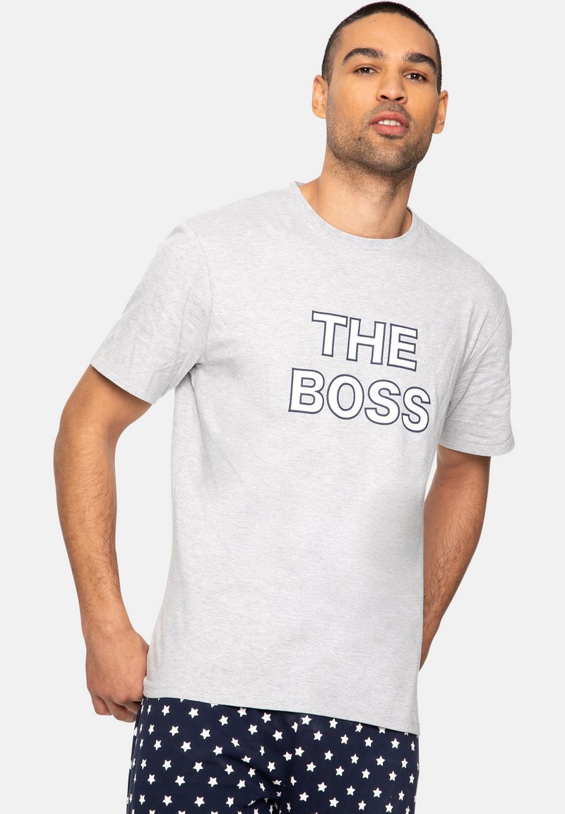 Graues Baumwoll-T-Shirt mit dem bedruckten Text "DER CHEF" in fettem Marineblau. Kurze Ärmel und ein Rundhalsausschnitt, kombiniert mit Sternenmuster-Hosen.