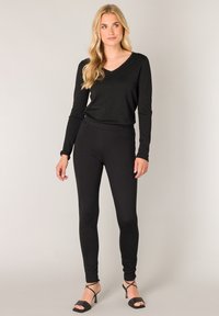 Zwarte langwerpige V-hals top in combinatie met zwarte leggings en strappy zwarte hakken. De outfit heeft een aansluitend ontwerp en een zachte textuur.