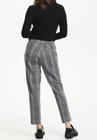 Pantalons à carreaux gris et noir avec une coupe slim, jambe fuselée et poches arrière. Portés avec un haut noir à manches longues et des chaussures noires épaisses.