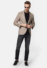 Beżowy marynarka o fakturze z dopasowanym krojem, noszona z czarnym T-shirtem i ciemnymi dżinsami. W połączeniu z czarnymi trampkami i okularami przeciwsłonecznymi.