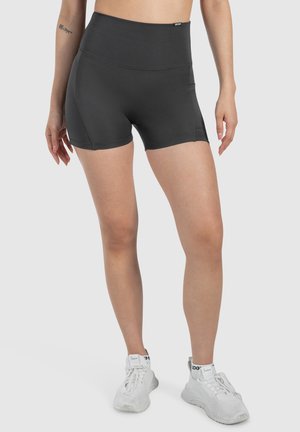 Shorts atletici neri a vita alta con un design senza cuciture, texture liscia e un dettaglio con tasca laterale per maggiore comodità, indossati con sneaker bianche.