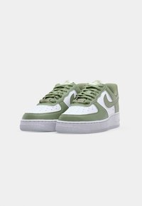 Hvide og grønne lædersneakers med polstret krave, teksturerede sideskaller, snørering foran og gummisål. Nike-logo på siden.