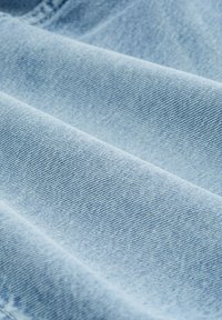Világoskék denim anyag sima textúrával és jellegzetes diagonális szövésmintával, lágy redőkkel és gyűrődésekkel.