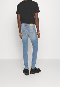 Ljusblå jeans med smal passform i denim med slät yta, femficksdesign och brunt läderlappar bak. Kombineras med en svart t-shirt och svarta stövlar.