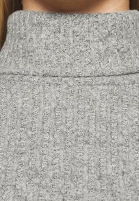 Maglione grigio a dolcevita con una trama a coste e strisce verticali. Il tessuto appare morbido e ha una leggera lucentezza, con un collo alto.