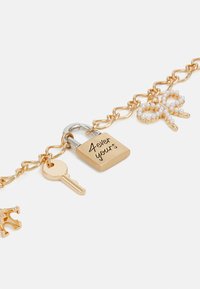 Guldtonet kædearmbånd med en hængelåscharms indgraveret med "4ever yours", en sølvnøgle, og en hvid perleprydet sløjfedetail.