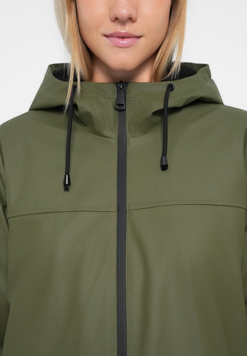 Olijfgroene waterdichte jas met een capuchon, zwarte rits en trekkoordjes, een gladde textuur en horizontale stiksels over de borst.
