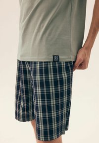 Zielony bawełniany t-shirt w połączeniu z granatowymi i jasnozielonymi szortami w kratę. Posiada płaskie szwy oraz małą metkę marki po boku szortów.