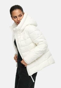 Witte pufferjack met een grote capuchon, ritssluiting en een doorgestikt patroon. Voorzien van trekkoorden en een logo-accent op de mouw.