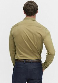 Olijfgroen langemouwen-shirt met een rechte snit, geknoopte manchetten en schouderpand, gecombineerd met donkerblauwe broeken en een geweven bruine riem.