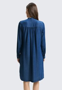 Robe en denim, à manches longues, couleur bleu royal, design froncé à l'arrière, col et poignets boutonnés, tombe à mi-cuisse, texture douce.