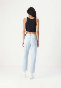 Top corto nero, jeans a vita alta blu chiaro e scarpe bianche con calzini bianchi. I jeans presentano una texture sbiadita e due tasche posteriori.