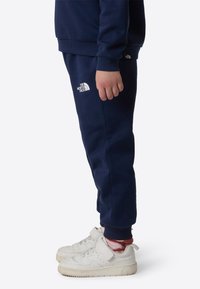 Marineblå genser og bukser laget av mykt stoff, med The North Face-logo i hvitt; kombinert med hvite joggesko og mønstrede sokker.