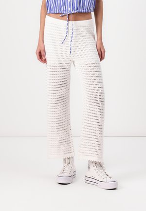 Pantalons larges en crochet blanc avec une texture tricotée. Associés à des baskets montantes blanches. Coupe décontractée avec une taille élastique.