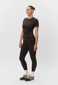 Brązowy zestaw odzieży sportowej z dopasowaną bluzką z krótkim rękawem i legginsami z wysokim stanem, w zestawieniu z brązowymi butami sportowymi i białymi skarpetkami do kostek.