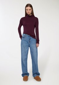 Bordowy sweter z golfem w połączeniu ze jasnoniebieskimi, szerokimi dżinsami i brązowym obuwiem sięgającym kostek. Prosty, luźny fason.