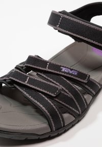 Sort Teva sandal med tre justerbare remme, grå polstret sål og tekstureret gummi ydersål. Har lilla logo på remmen.