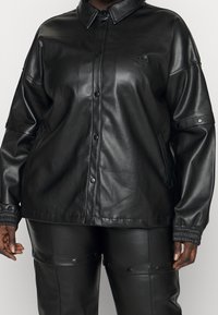 Svart fodrad läderjacka med krage, tryckknappar, sidfickor och ribbade ärmslut. Har subtilt varumärkeslogotyp på bröstet.