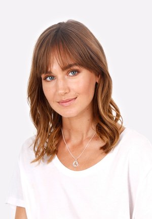 Sølvvedhængs halskæde på en tynd kæde båret over en hvid bluse. Modellen har skulderlangt bølget brunt hår og ingen makeup.