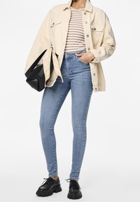 Beige denimjacka, randig brun och vit topp, ljusblå skinny jeans, svarta klumpiga skor och en svart väska med en mönstrad scarf.