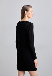 Abito in rete nera con maniche lunghe, scollatura rotonda e silhouette aderente. La texture è leggera con un sottile motivo a trama aperta.