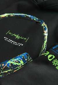Zwarte hoodie met heldere blauwe, groene en oranje grafische elementen, tekst en een cirkelontwerp. Glad van textuur met een casual pasvorm.