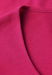 Fuksjowa bawełniana tkanina o gładkiej fakturze; ma okrągły dekolt i widoczne szwy wokół kołnierza.