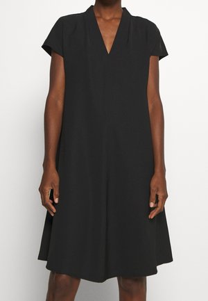 Czarna sukienka bez rękawów z dekoltem w serek i luźnym krojem w linii A, noszona przez osobę o ciemnej karnacji, pokazana od szyi do kolan.