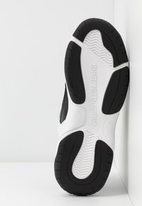 Baskets noir et blanc avec surface texturée, semelle en caoutchouc et marquage "CALVIN KLEIN JEANS" bien visible sur le talon.