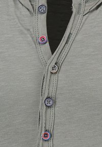 Grijze button-up overhemd met een v-halslijn en vijf veelkleurige knopen, zachte textuur en gestikte details langs de knoopsluiting.