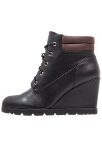 Bottines à talon compensé en cuir noir avec un col rembourré marron, un laçage à l'avant avec œillets en métal et une semelle en caoutchouc texturé.