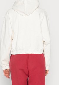 Vit croppad hoodie med huva, med en texturerad yta och elastisk midja. Matchas med röda sweatpants.