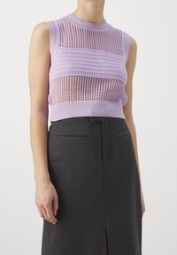 Lyhyt, hihaton paita, joka on valmistettu purppuran värisestä neulotusta kankaasta, jossa on teksturoitu kuvio. Tyylitetty korkealla kauluksella, yhdistetty harmaisiin hameisiin.