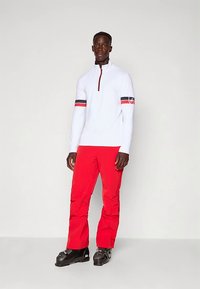 Weißer Langarm-Quarter-Zip-Sweatshirt mit roten und navyblauen Streifen an den Ärmeln, kombiniert mit roten Hosen und schwarzen Stiefeln.