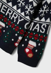 Pullover lavorato a maglia blu navy con fiocchi di neve bianchi, calze di Natale rosse, dettagli verdi e testo "BUON NATALE" in grassetto bianco.