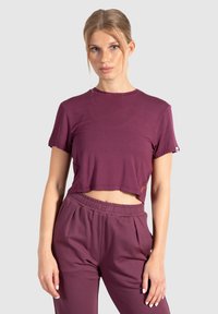 Bordeauxkleurig cropped t-shirt met korte mouwen, een gladde textuur, ronde halslijn en subtiele logo-detail op de zoom, gecombineerd met bijpassende joggers.