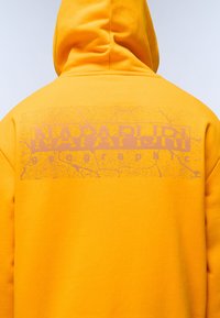 Felpa gialla brillante con stampe grafiche di un giallo più chiaro sul retro, che mostra il testo "NAPAPIJRI geographic." Texture liscia.