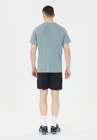 Harmaan lyhythihaisen urheilupaidan, mustien shortsien ja mustien juoksukenkiä. Paidassa on pyöreä kaulus ja yksinkertainen muotoilu.